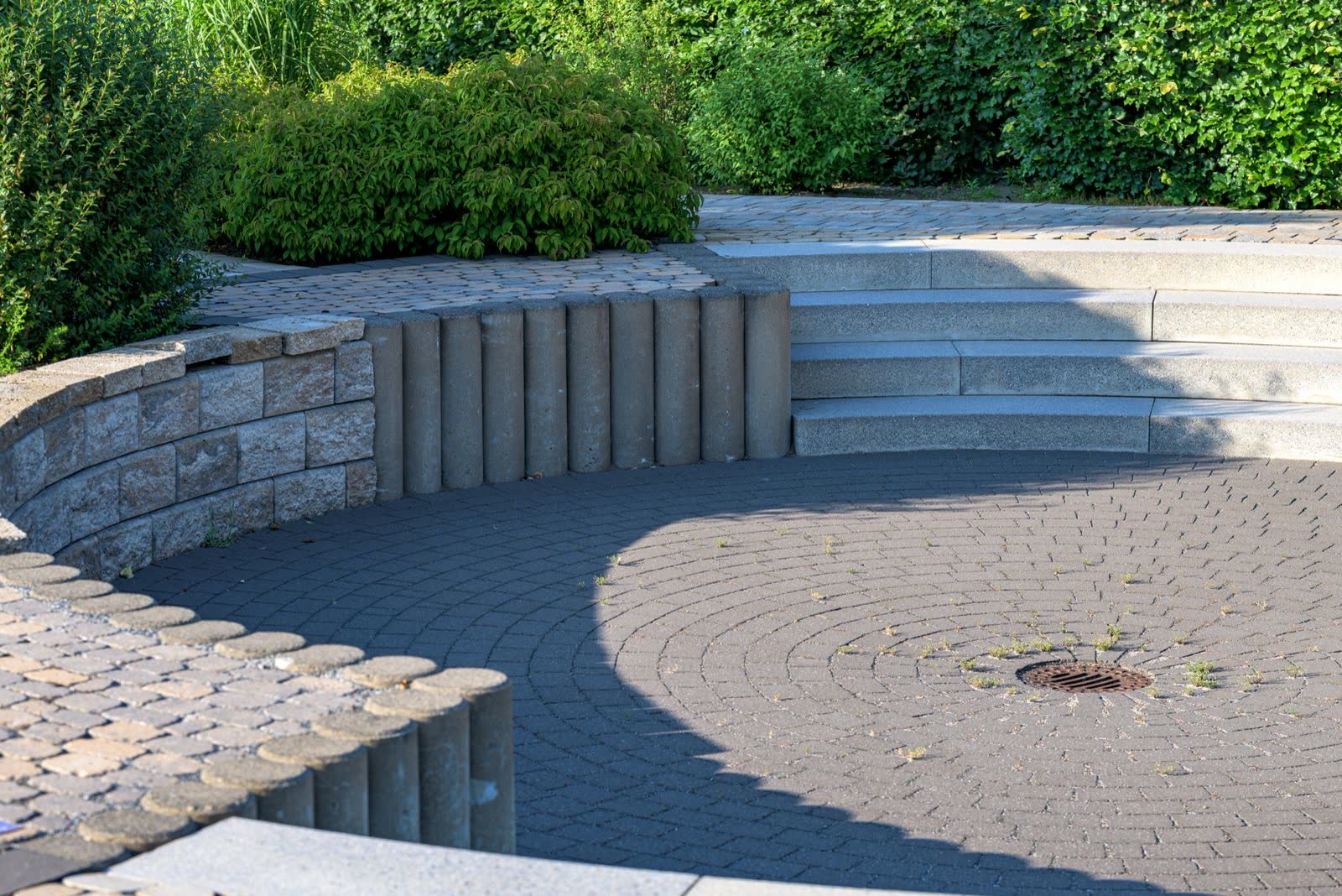 A segmental block retaining wall curving around a paved area with steps